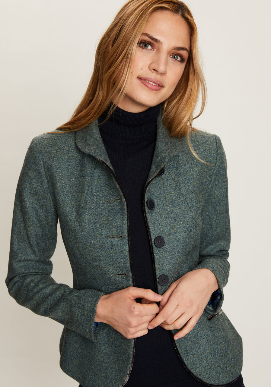 Woman wearing a teal jacket over a black turtleneck on a plain background