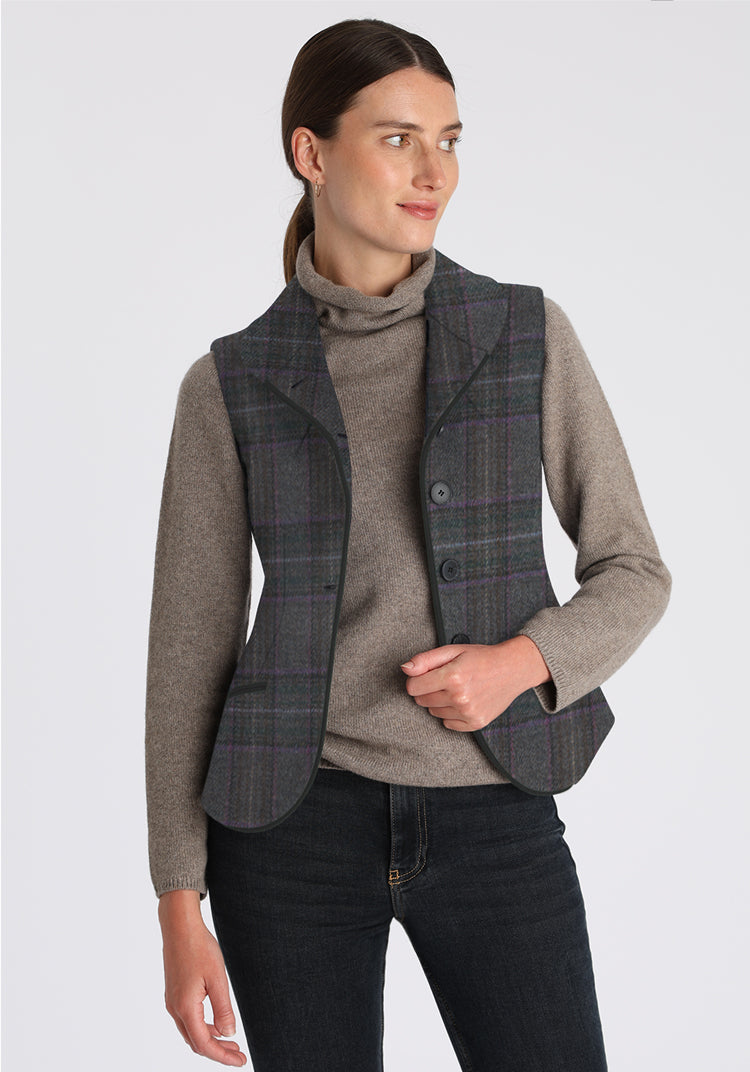 Woman wearing a purple and gray waistcoat with plaid pattern over a gray sweater on a light gray background