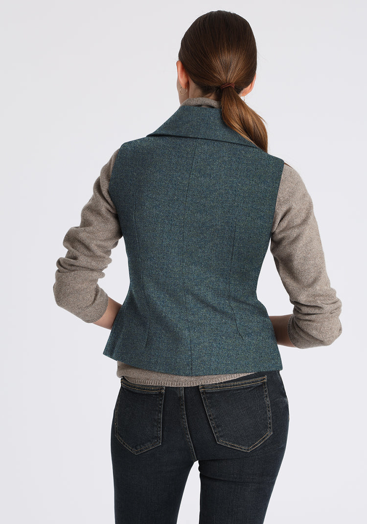 Person wearing a teal waistcoat over a gray shirt with black pants on a white background