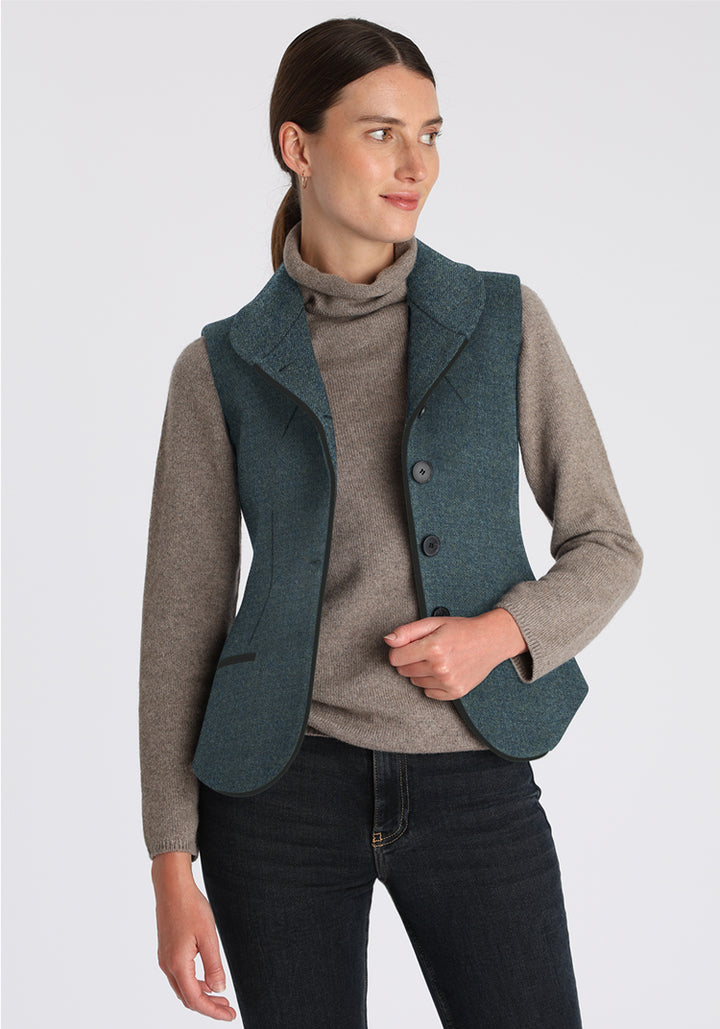 Woman wearing a teal waistcoat over a gray sweater on a light gray background