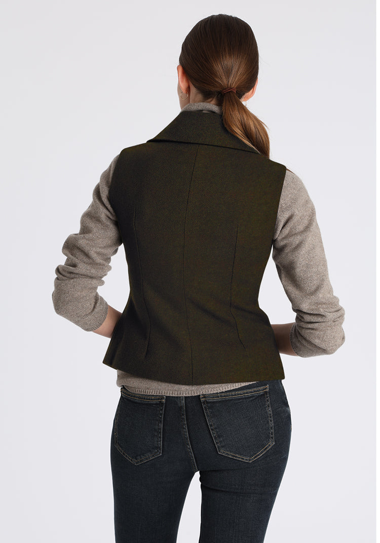 Person wearing a green vest over a gray shirt and jeans on a white background