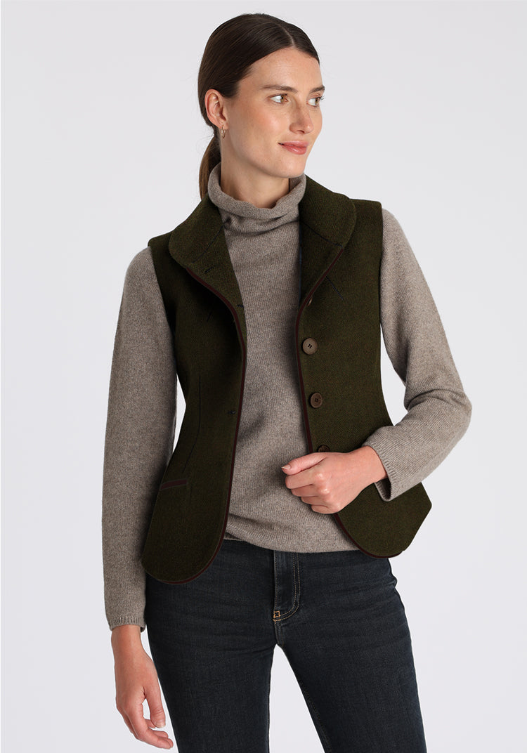 Woman wearing a forest green vest over a gray sweater on a light gray background