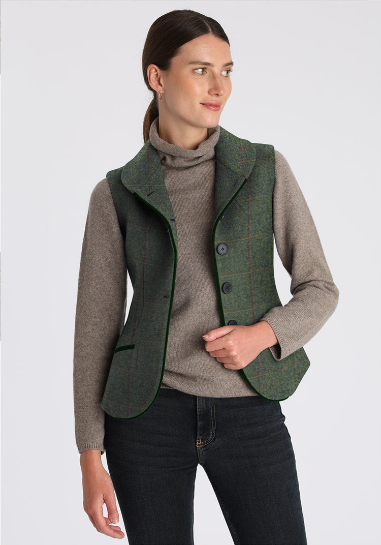 Woman wearing a green waistcoat over a gray sweater on a white background