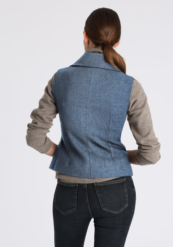 Woman wearing a blue waistcoat over a grey sweater on a grey background