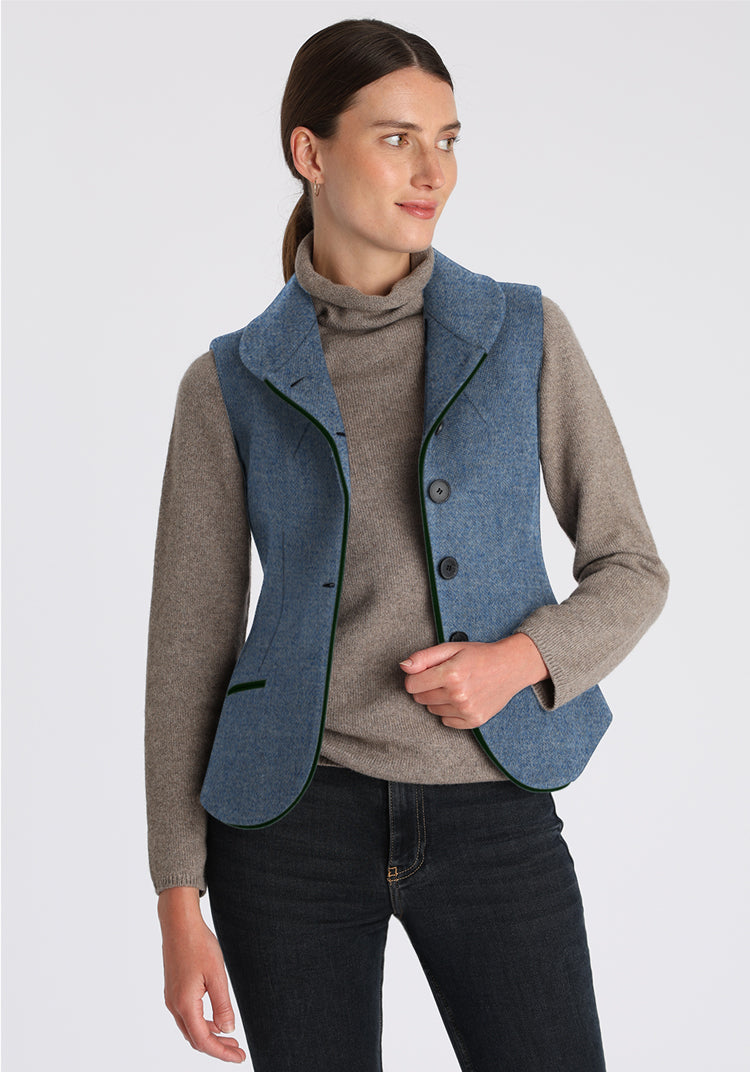 Woman wearing a blue waistcoat over a grey sweater on a grey background