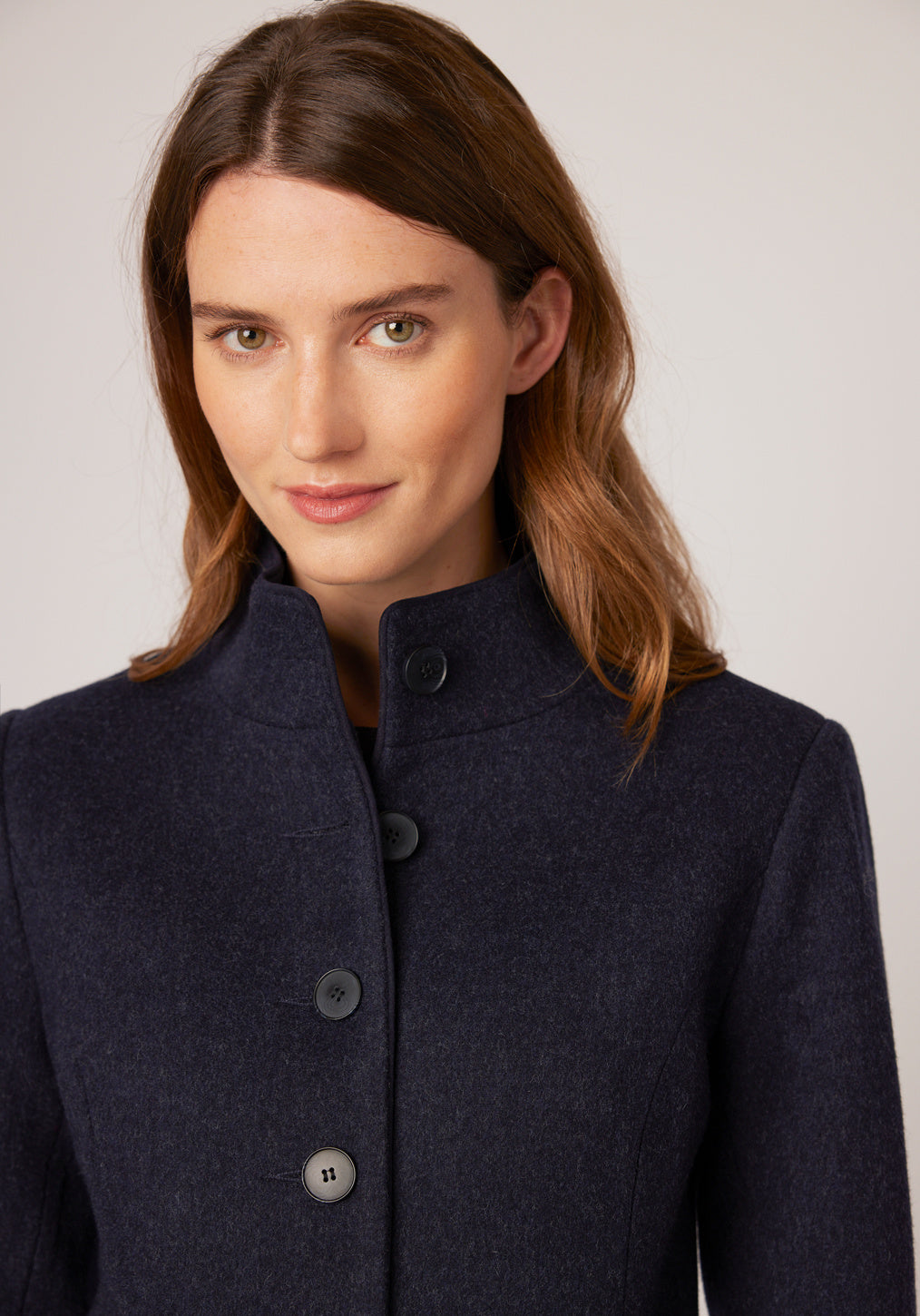 A model wears the Opera coat, a fitted, longline coat made from thick navy marl merino wool with navy suede trim.