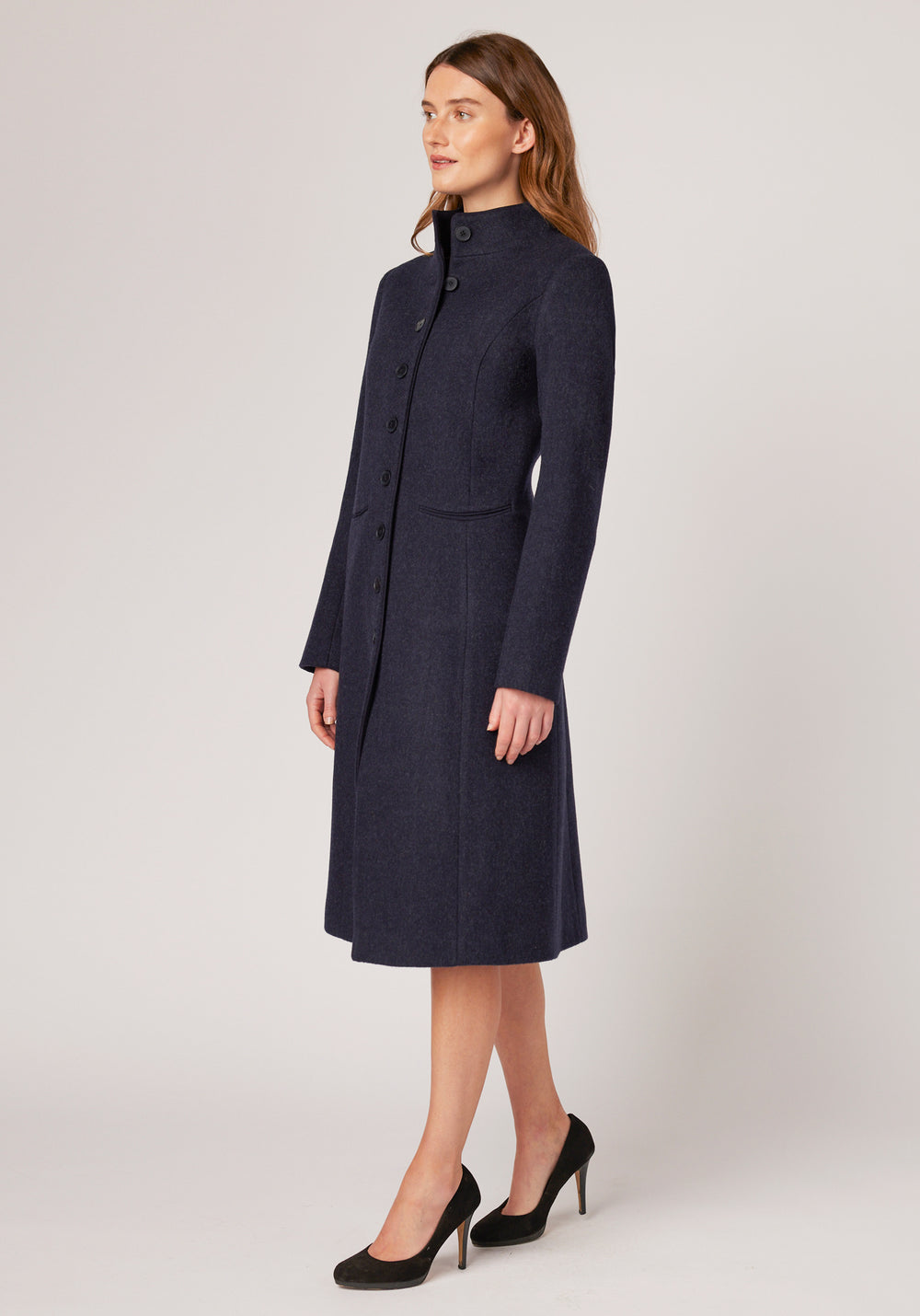 A model wears the Opera coat, a fitted, longline coat made from thick navy marl merino wool with navy suede trim.