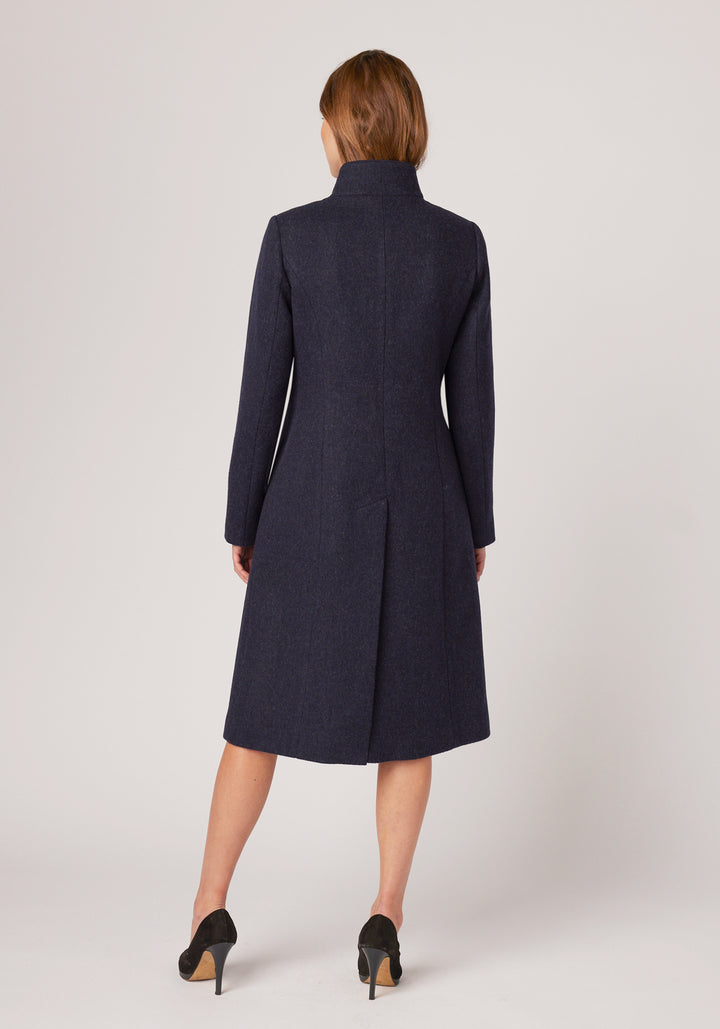 A model wears the Opera coat, a fitted, longline coat made from thick navy marl merino wool with navy suede trim.