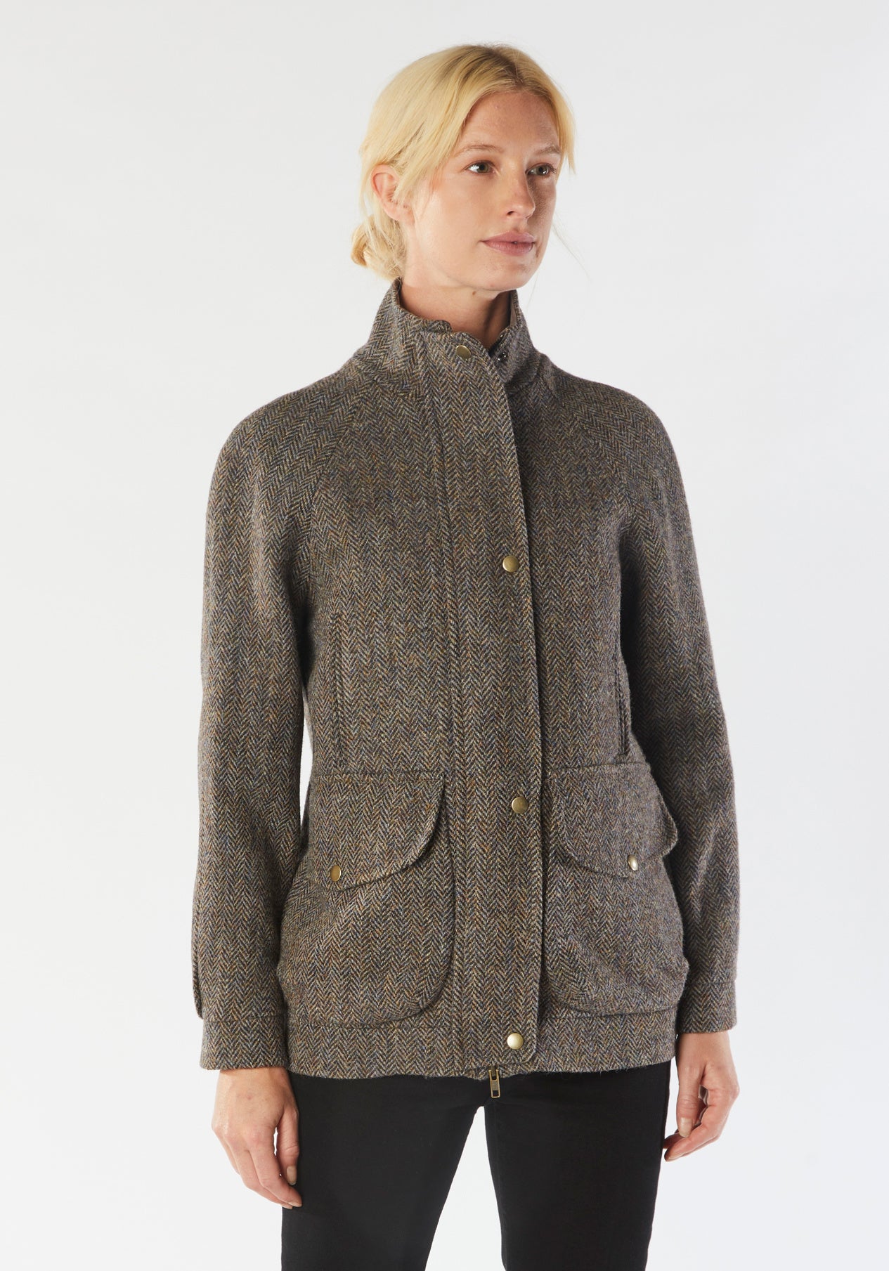 A model wears the Andrea jacket in Harris Tweed, featuring relaxed raglan sleeves, a high neck, generous pockets, and finished with antique brass hardware.