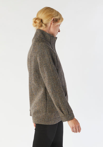 A model wears the Andrea jacket in Harris Tweed, featuring relaxed raglan sleeves, a high neck, generous pockets, and finished with antique brass hardware.