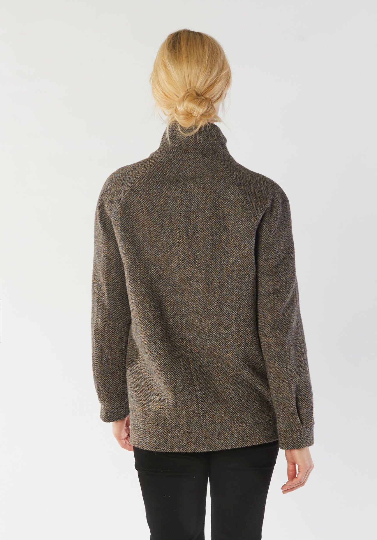 A model wears the Andrea jacket in Harris Tweed, featuring relaxed raglan sleeves, a high neck, generous pockets, and finished with antique brass hardware.