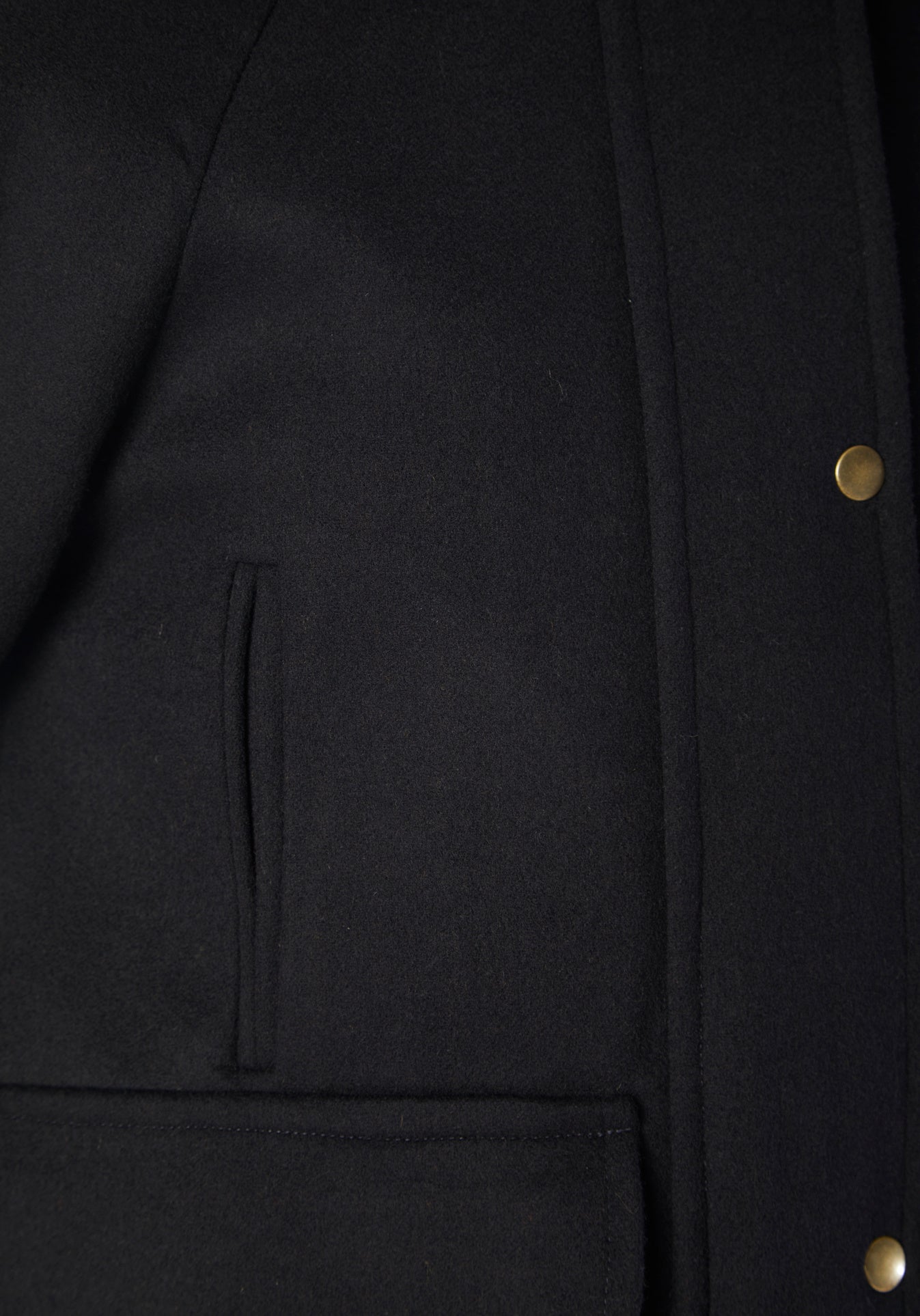 A model wears the Andrea jacket in navy merino wool, featuring relaxed raglan sleeves, a high neck, generous pockets, and finished with antique brass hardware.