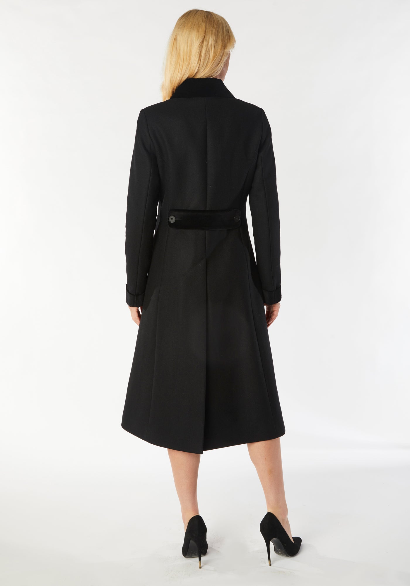 A model wears the Contrast Coat, a long and elegantly tailored black wool cashmere coat with black cotton velvet accents on the collar, cuffs, back belt, and pocket flaps.