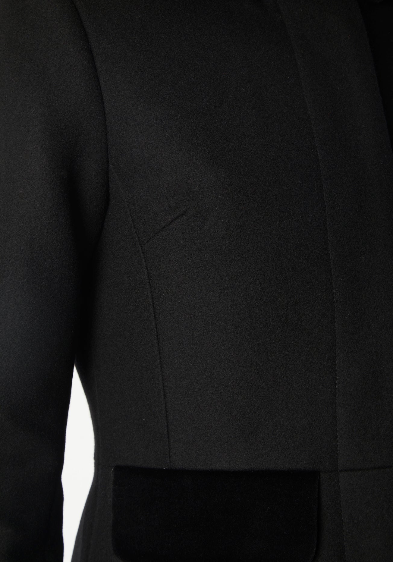 A model wears the Contrast Coat, a long and elegantly tailored black wool cashmere coat with black cotton velvet accents on the collar, cuffs, back belt, and pocket flaps.