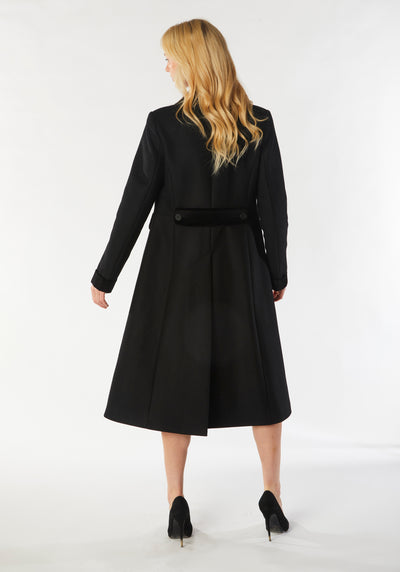 A model wears the Contrast Coat, a long and elegantly tailored black wool cashmere coat with black cotton velvet accents on the collar, cuffs, back belt, and pocket flaps.
