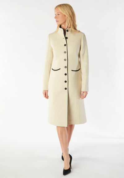 A model wears the Opera coat, a fitted, longline coat made from thick cream merino wool with black contrasting trim.
