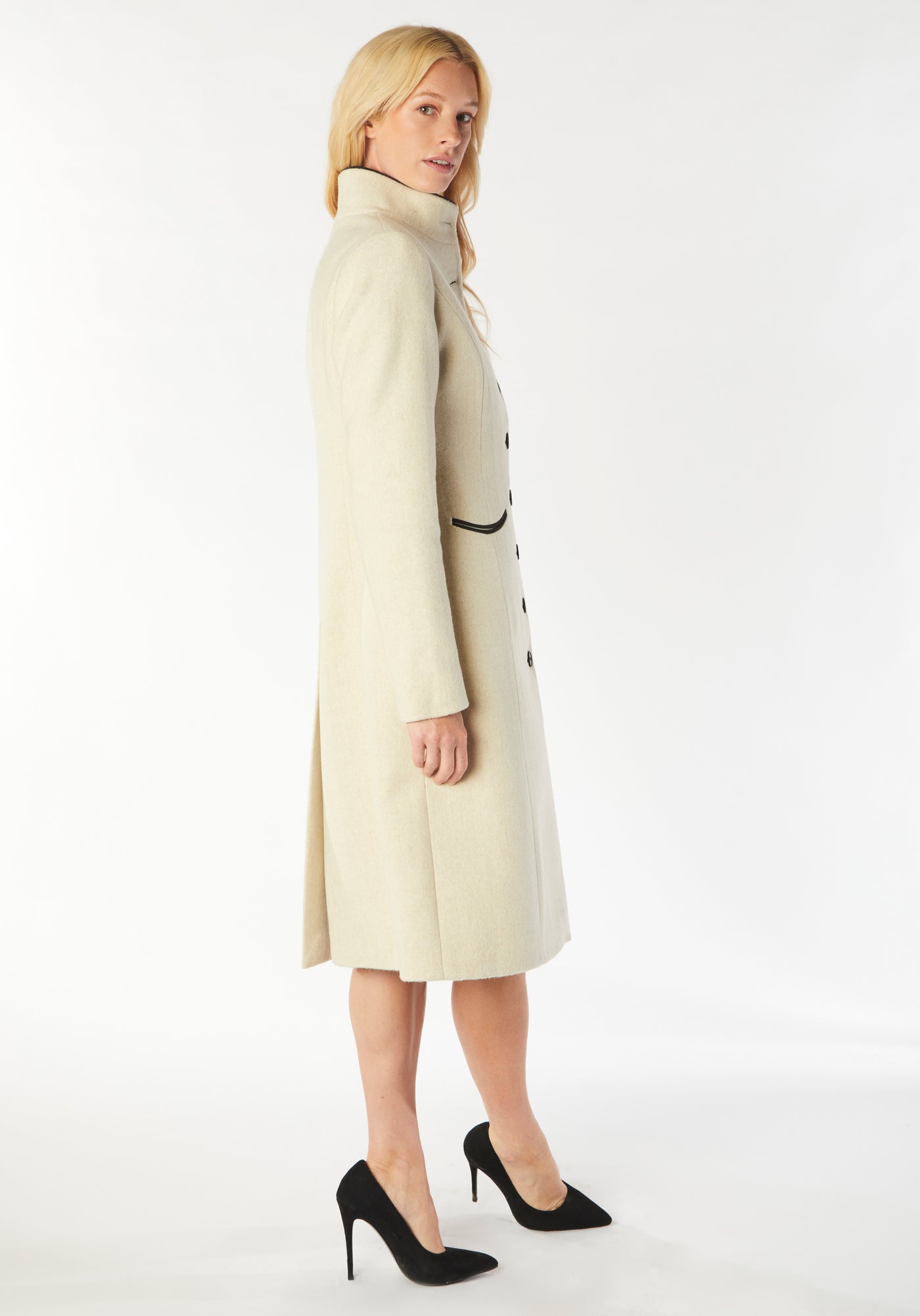 A model wears the Opera coat, a fitted, longline coat made from thick cream merino wool with black contrasting trim.