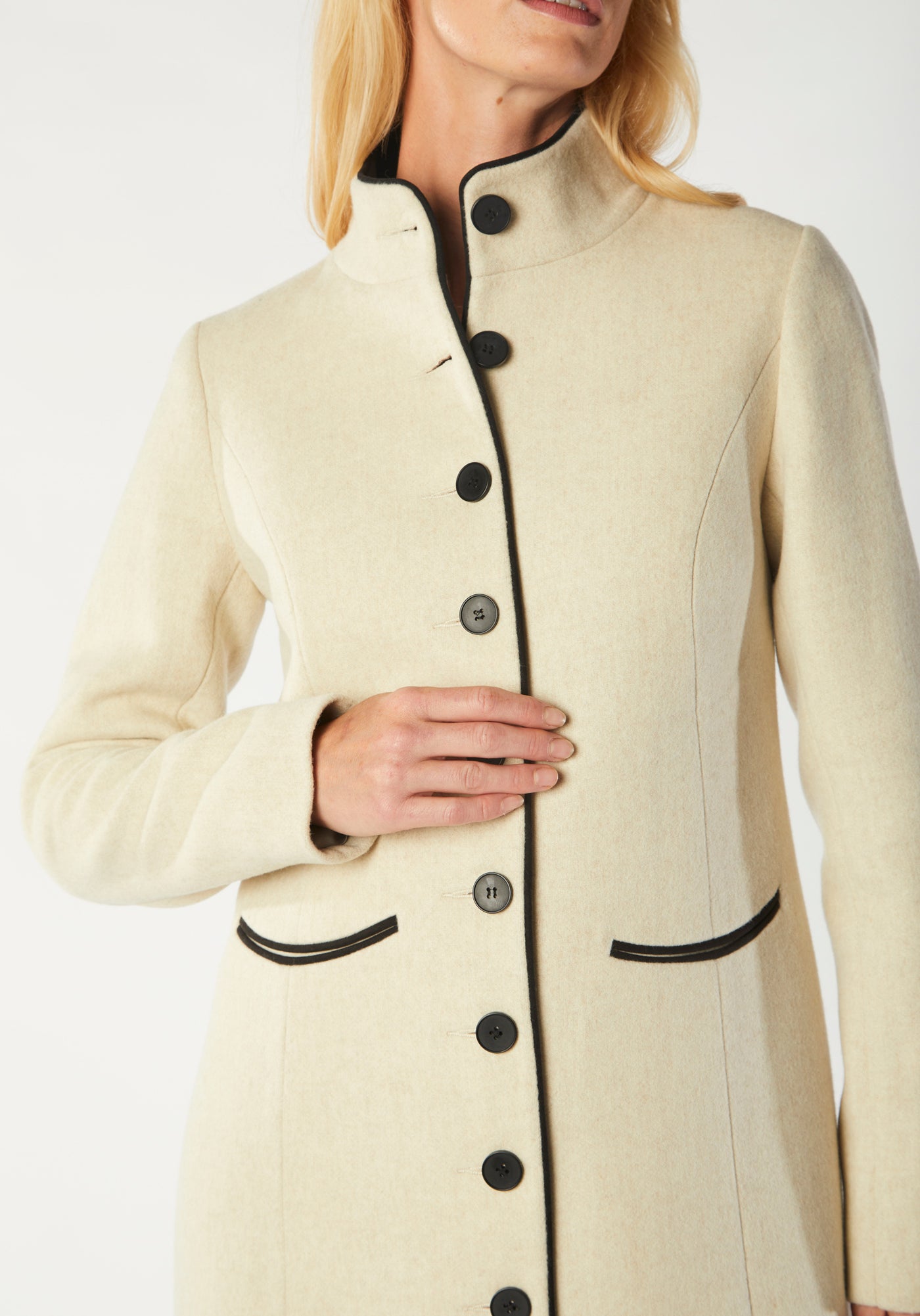A model wears the Opera coat, a fitted, longline coat made from thick cream merino wool with black contrasting trim.