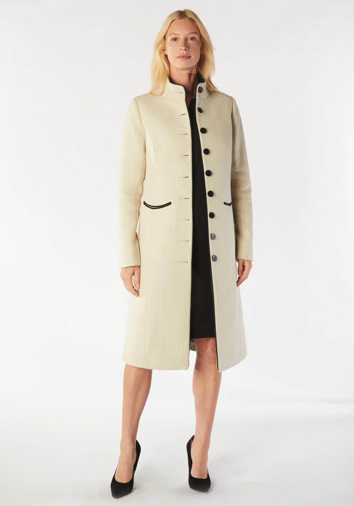 A model wears the Opera coat, a fitted, longline coat made from thick cream merino wool with black contrasting trim.