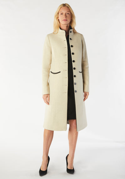 A model wears the Opera coat, a fitted, longline coat made from thick cream merino wool with black contrasting trim.