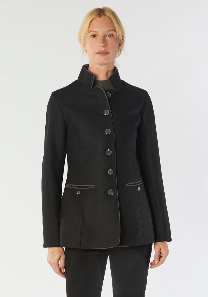 A model wears the Patmos Jacket, a slim-fit design in a black cashmere blend with contrasting grey trim. It features a mandarin collar, front pockets, and deep cuffs with a row of charcoal buttons.