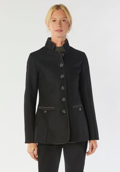 A model wears the Patmos Jacket, a slim-fit design in a black cashmere blend with contrasting grey trim. It features a mandarin collar, front pockets, and deep cuffs with a row of charcoal buttons.