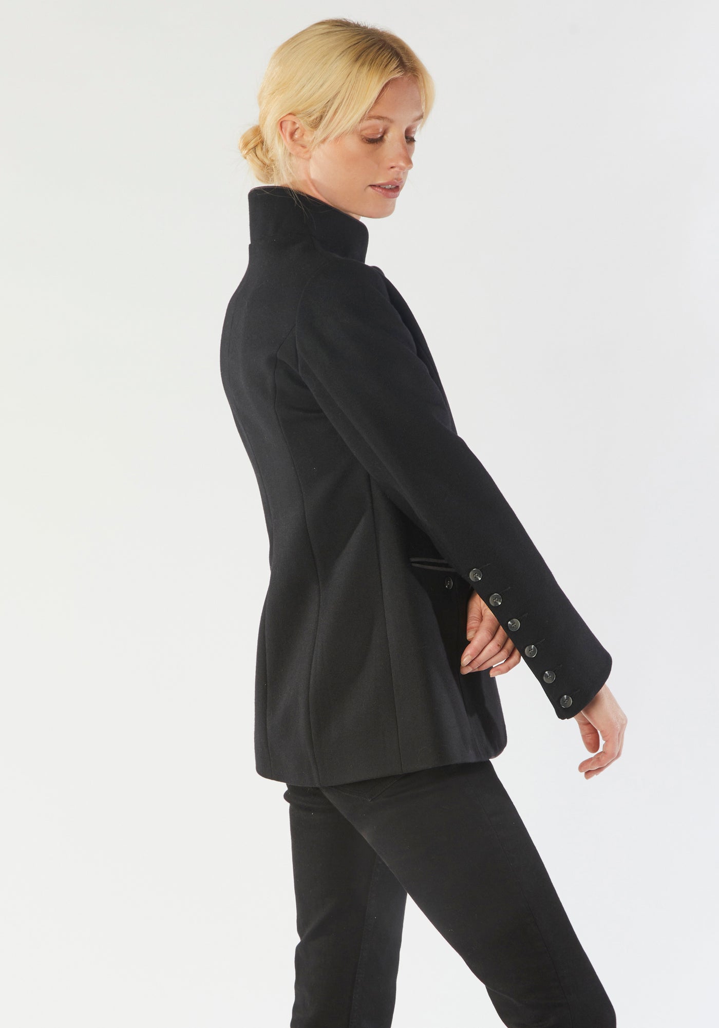 A model wears the Patmos Jacket, a slim-fit design in a black cashmere blend with contrasting grey trim. It features a mandarin collar, front pockets, and deep cuffs with a row of charcoal buttons.