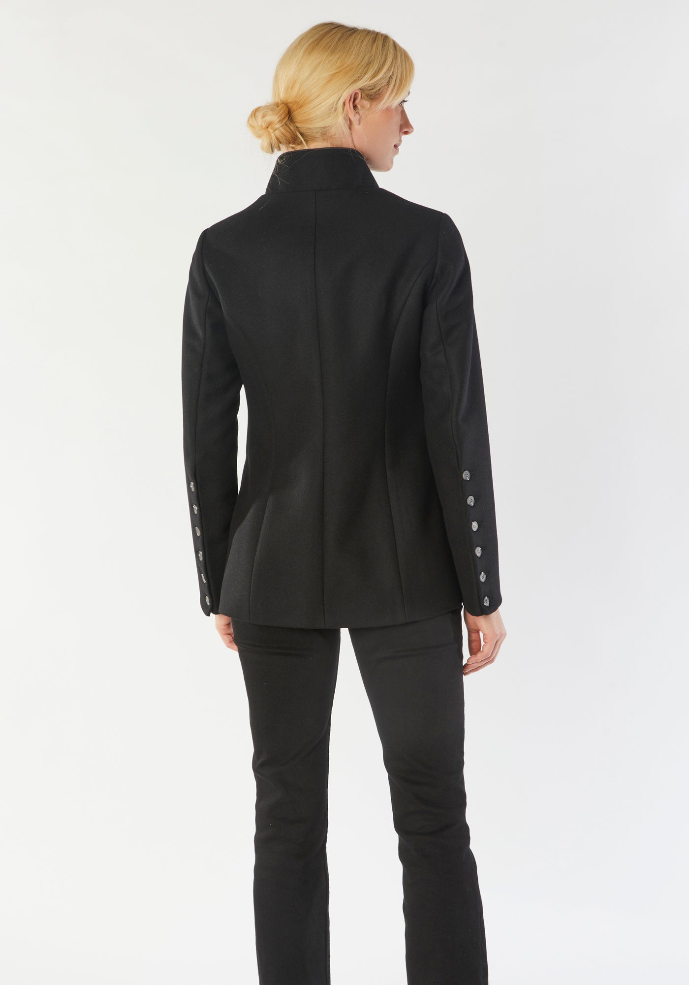 A model wears the Patmos Jacket, a slim-fit design in a black cashmere blend with contrasting grey trim. It features a mandarin collar, front pockets, and deep cuffs with a row of charcoal buttons.