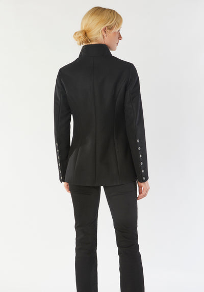 A model wears the Patmos Jacket, a slim-fit design in a black cashmere blend with contrasting grey trim. It features a mandarin collar, front pockets, and deep cuffs with a row of charcoal buttons.