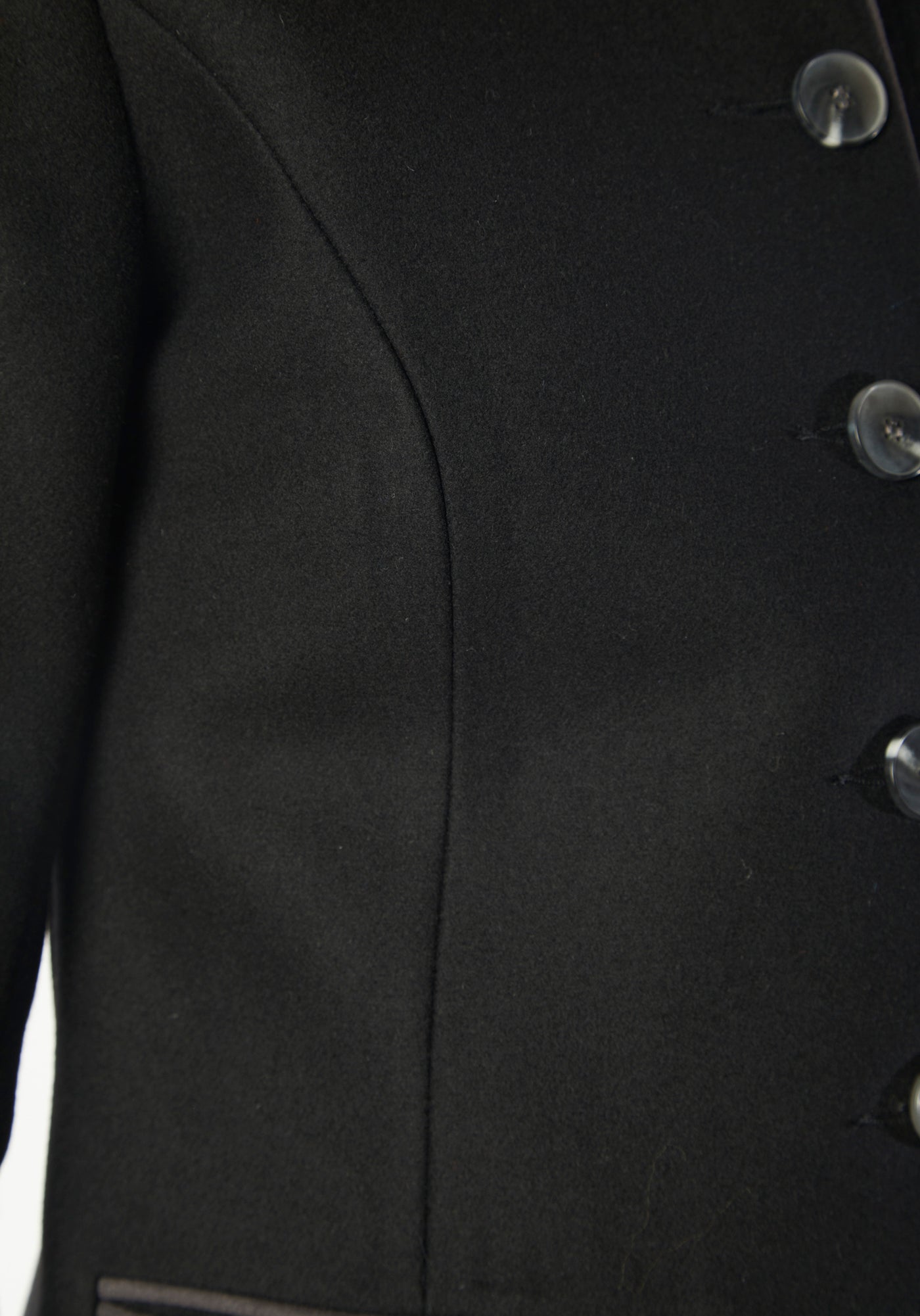 A model wears the Patmos Jacket, a slim-fit design in a black cashmere blend with contrasting grey trim. It features a mandarin collar, front pockets, and deep cuffs with a row of charcoal buttons.
