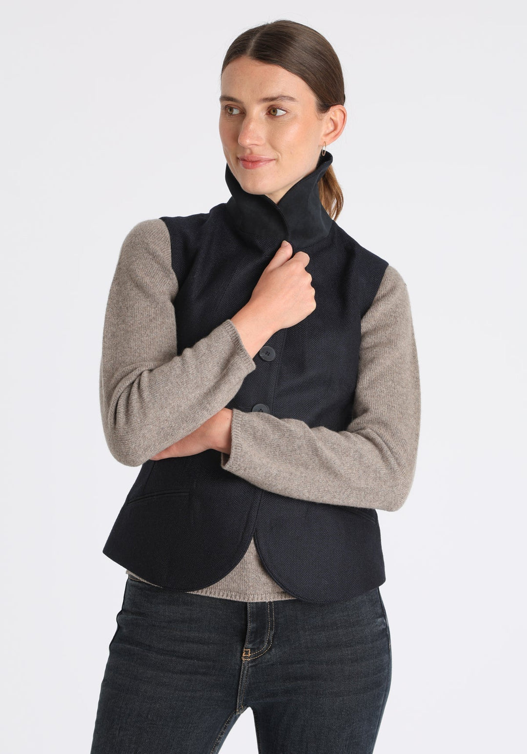 Model wearing the Alexander waistcoat in a navy herringbone lambswool, a short, fitted style with a shawl collar, suede trim, and curved front hem.