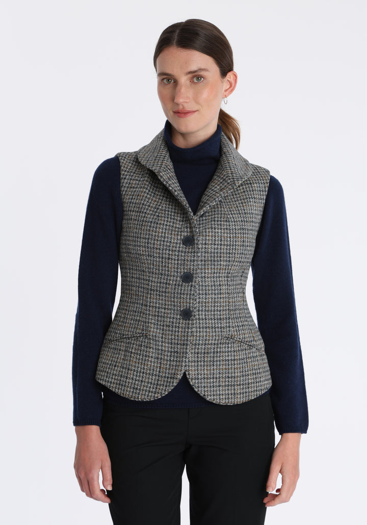 Model wearing the Alexander waistcoat in a stone grey and ochre dogtooth check wool, a short, fitted style with a shawl collar, silk velvet trim, and curved front hem.