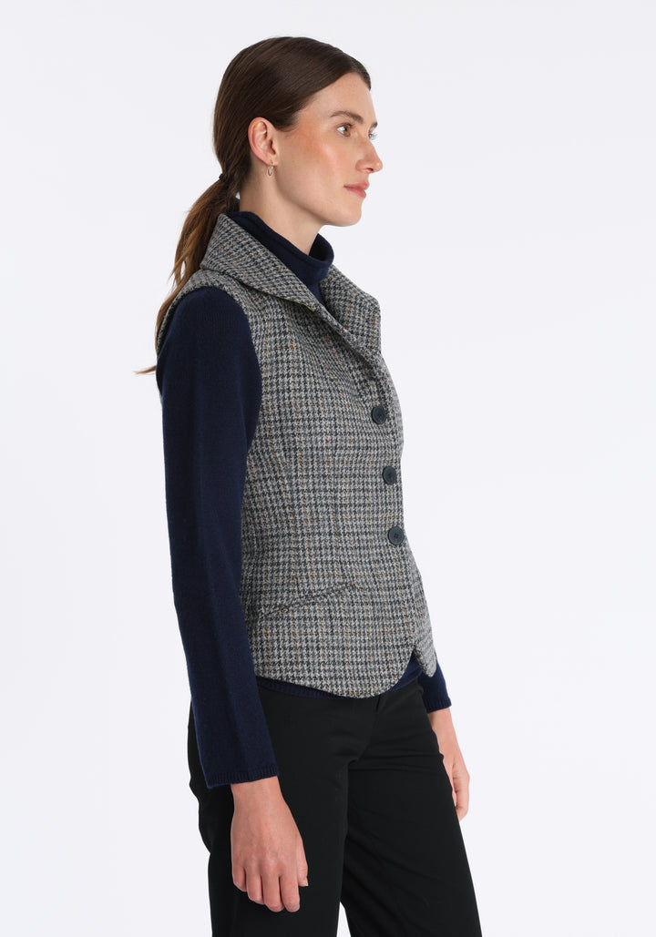 Model wearing the Alexander waistcoat in a stone grey and ochre dogtooth check wool, a short, fitted style with a shawl collar, silk velvet trim, and curved front hem.