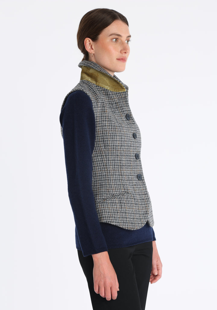 Model wearing the Alexander waistcoat in a stone grey and ochre dogtooth check wool, a short, fitted style with a shawl collar, silk velvet trim, and curved front hem.