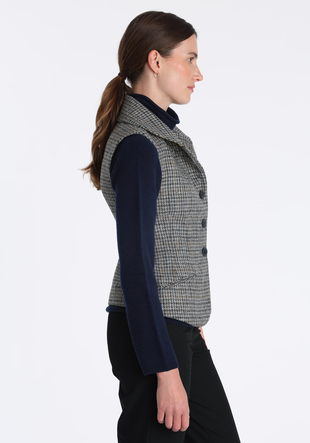 Model wearing the Alexander waistcoat in a stone grey and ochre dogtooth check wool, a short, fitted style with a shawl collar, silk velvet trim, and curved front hem.
