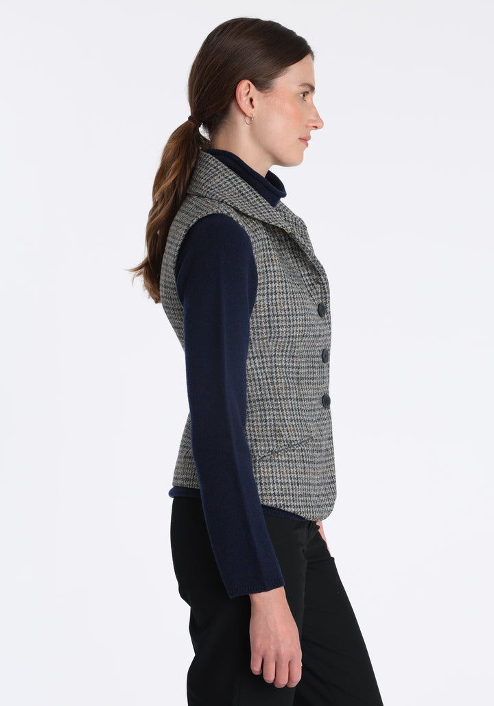 Model wearing the Alexander waistcoat in a stone grey and ochre dogtooth check wool, a short, fitted style with a shawl collar, silk velvet trim, and curved front hem.