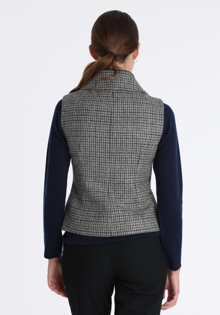 Model wearing the Alexander waistcoat in a stone grey and ochre dogtooth check wool, a short, fitted style with a shawl collar, silk velvet trim, and curved front hem.