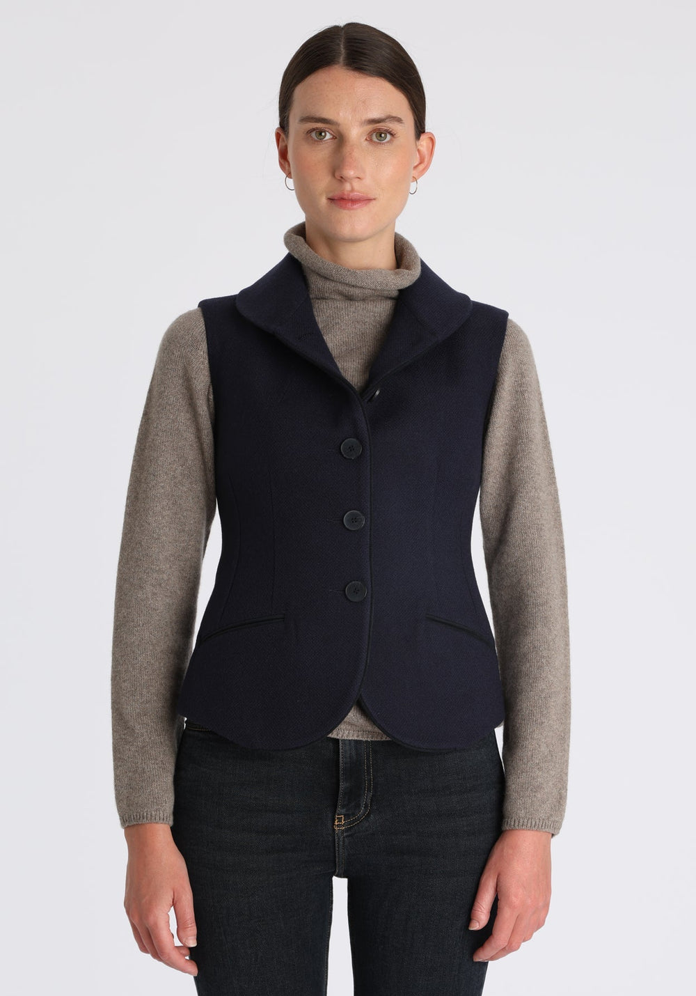 Model wearing the Alexander waistcoat in a textured navy merino wool, a short, fitted style with a shawl collar, suede trim, and curved front hem.
