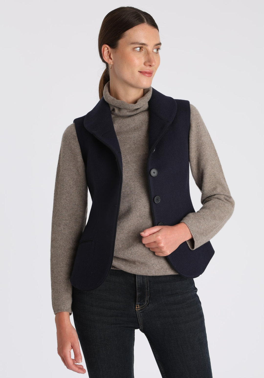 Model wearing the Alexander waistcoat in a textured navy merino wool, a short, fitted style with a shawl collar, suede trim, and curved front hem.