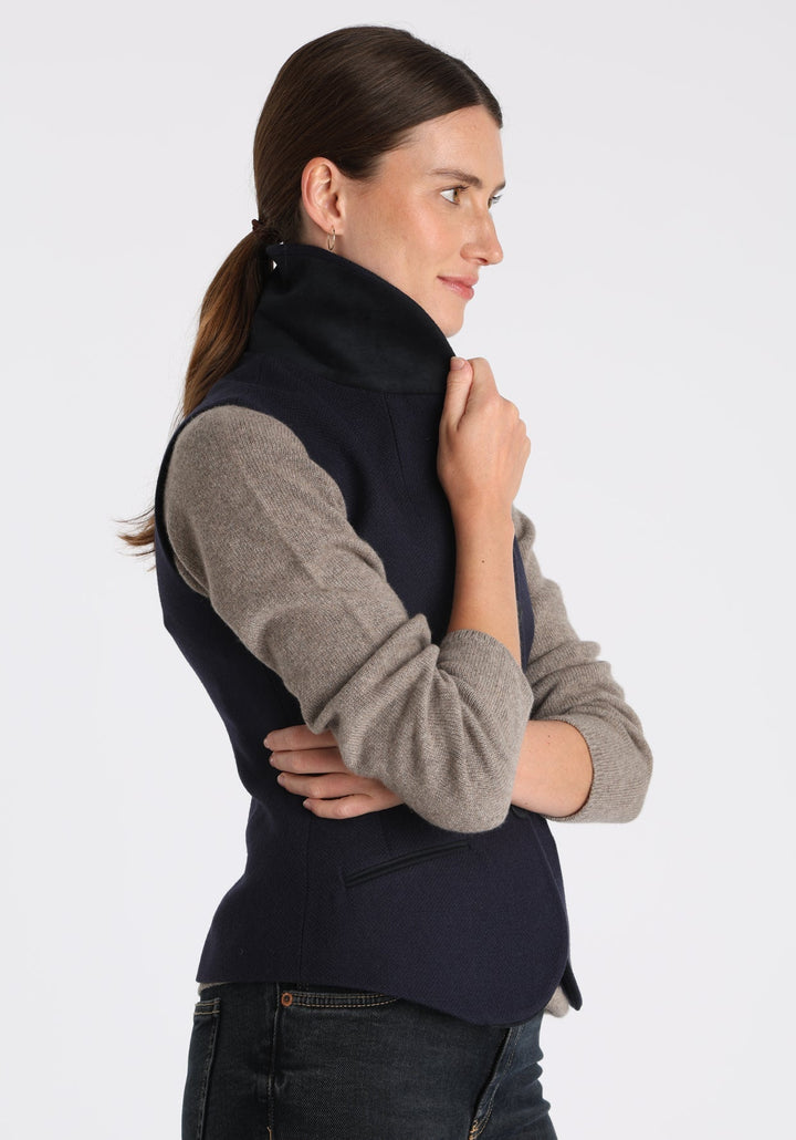 Model wearing the Alexander waistcoat in a textured navy merino wool, a short, fitted style with a shawl collar, suede trim, and curved front hem.