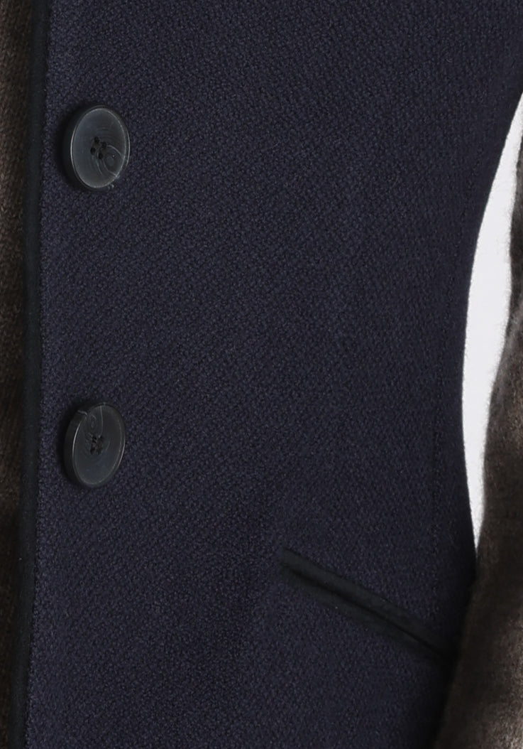 Model wearing the Alexander waistcoat in a textured navy merino wool, a short, fitted style with a shawl collar, suede trim, and curved front hem.