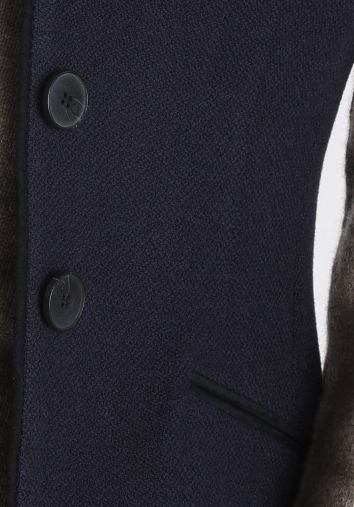 Model wearing the Alexander waistcoat in a textured navy merino wool, a short, fitted style with a shawl collar, suede trim, and curved front hem.