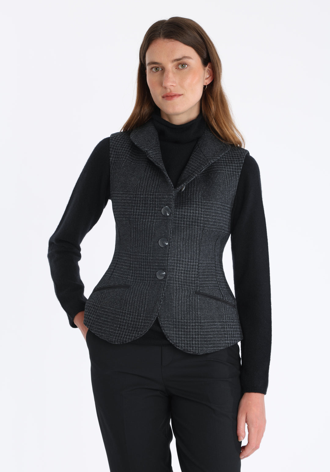 Model wearing the Alexander waistcoat in a black and charcoal grey Prince of Wales check, a short, fitted merino wool style with a shawl collar and curved front hem.