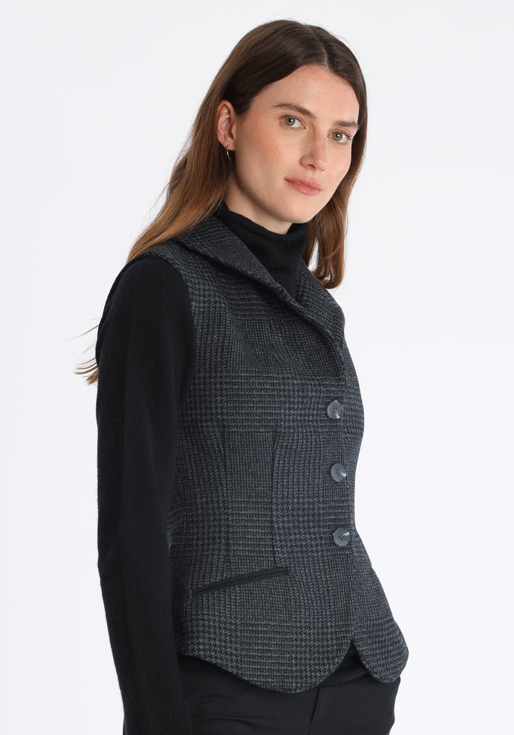 Model wearing the Alexander waistcoat in a black and charcoal grey Prince of Wales check, a short, fitted merino wool style with a shawl collar and curved front hem.