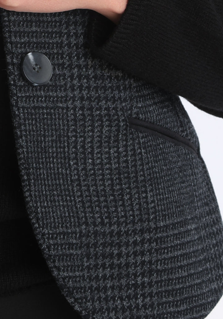 Model wearing the Alexander waistcoat in a black and charcoal grey Prince of Wales check, a short, fitted merino wool style with a shawl collar and curved front hem.