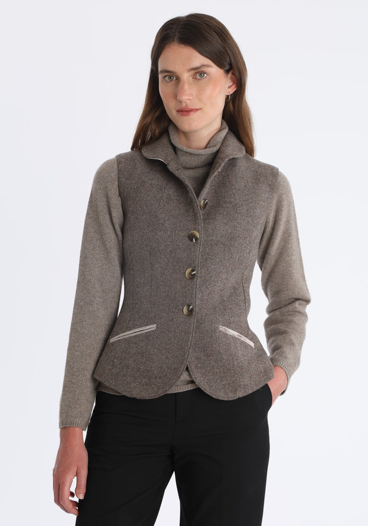 Model wearing the Alexander waistcoat in a cool mallow taupe herringbone lambswool, a short, fitted style with a shawl collar, silk velvet trim, and curved front hem.