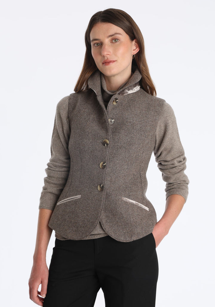 Model wearing the Alexander waistcoat in a cool mallow taupe herringbone lambswool, a short, fitted style with a shawl collar, silk velvet trim, and curved front hem.