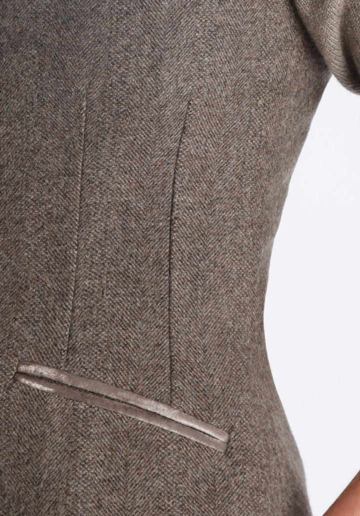 Model wearing the Alexander waistcoat in a cool mallow taupe herringbone lambswool, a short, fitted style with a shawl collar, silk velvet trim, and curved front hem.