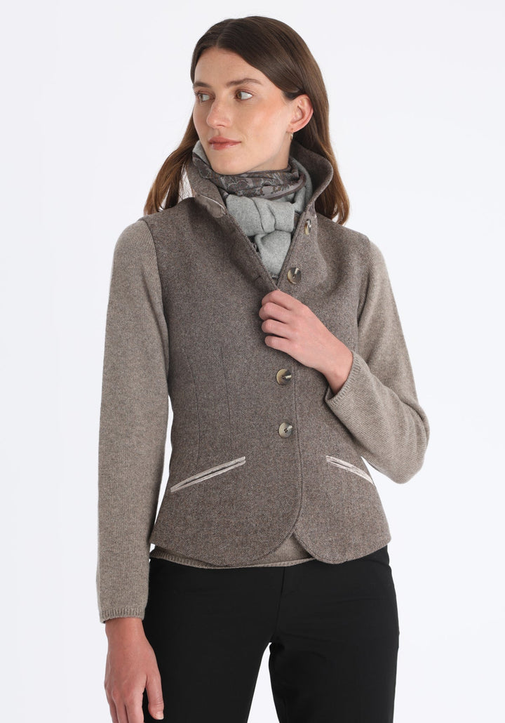 Model wearing the Alexander waistcoat in a cool mallow taupe herringbone lambswool, a short, fitted style with a shawl collar, silk velvet trim, and curved front hem.