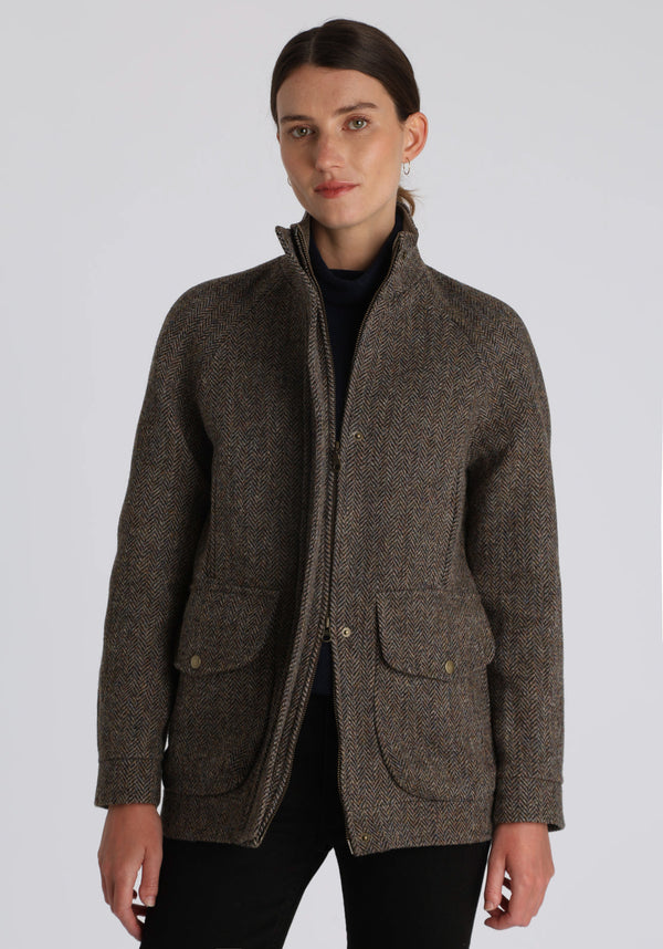 A model wears the Andrea jacket in Harris Tweed, featuring relaxed raglan sleeves, a high neck, generous pockets, and finished with antique brass hardware.